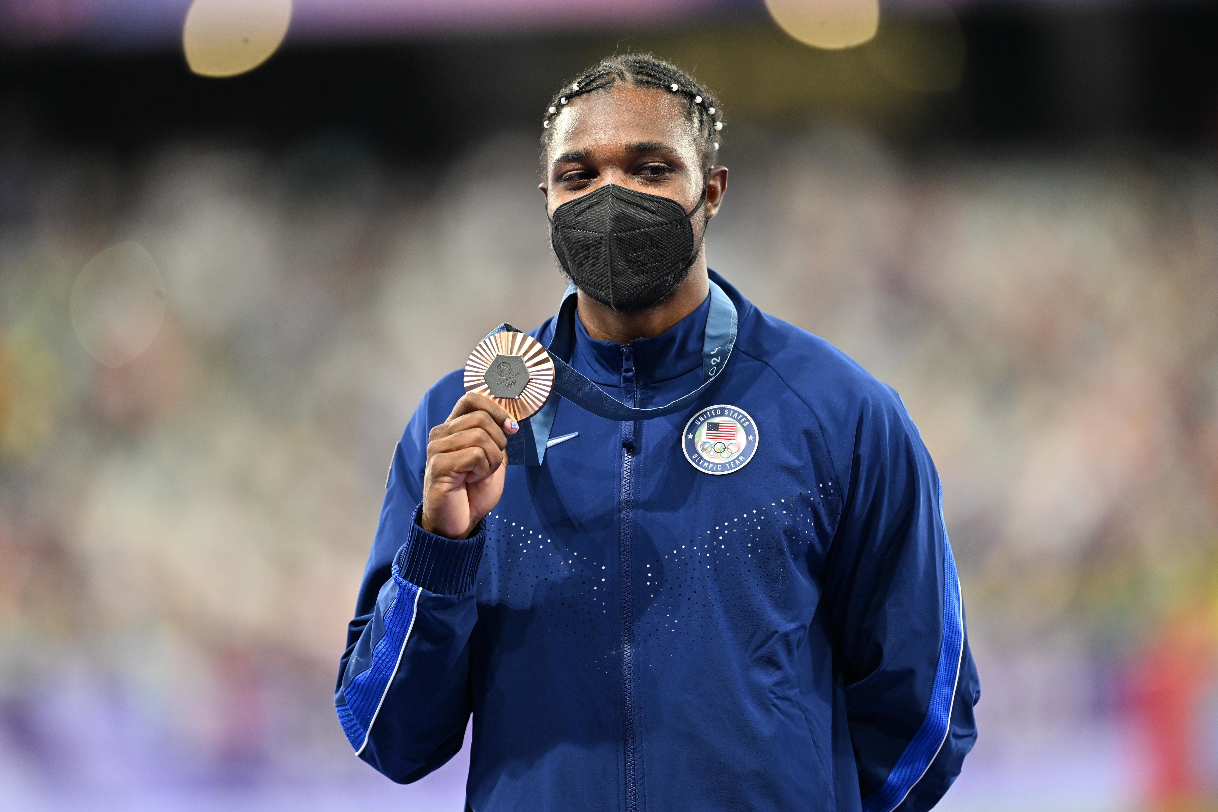 Athlete wearing a mask and a Team USA jacket holds a medal