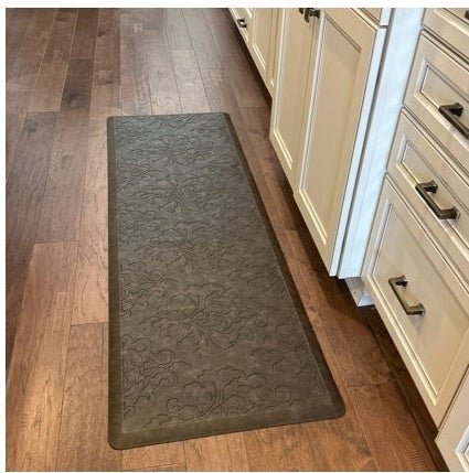 Kitchen with wood floor, cream cabinets, and an anti-fatigue mat with a detailed pattern. Article about shopping for home decor and kitchen essentials