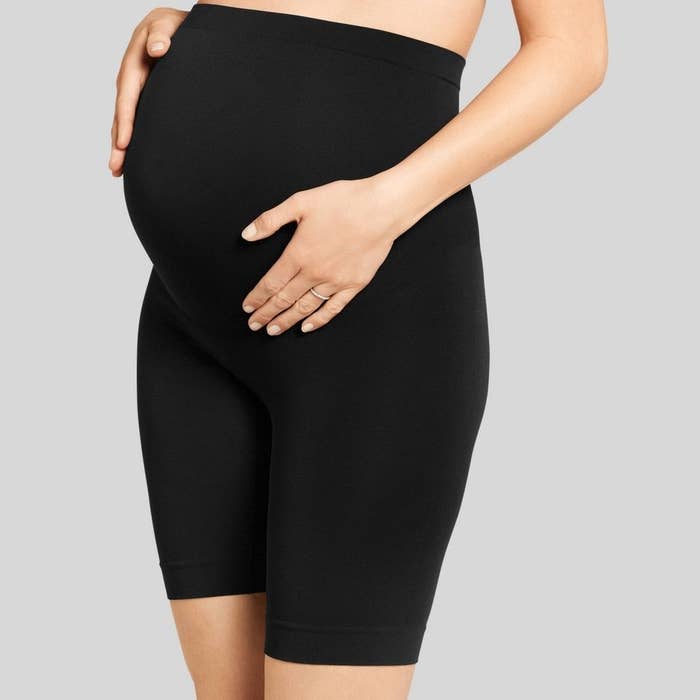 Person holding their pregnant belly while wearing black maternity shorts