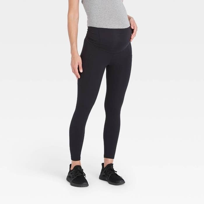 A person is modeling black maternity leggings and black athletic shoes. The model's face is not shown