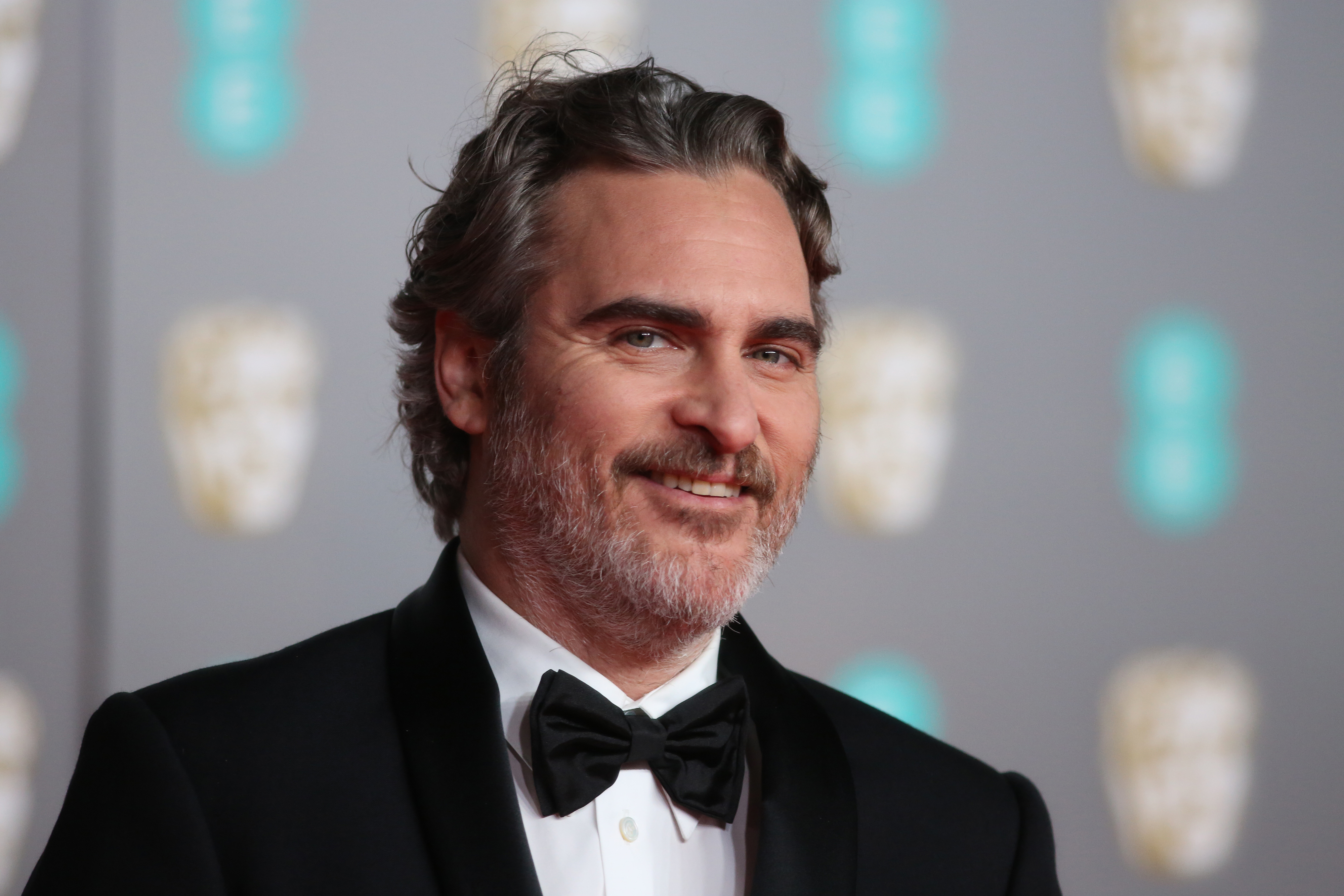 Joaquin Phoenix in a tuxedo smiles on the red carpet at a celebrity event