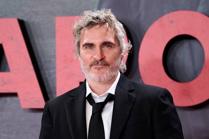 Joaquin Phoenix on the red carpet, wearing a dark suit and tie with a shirt