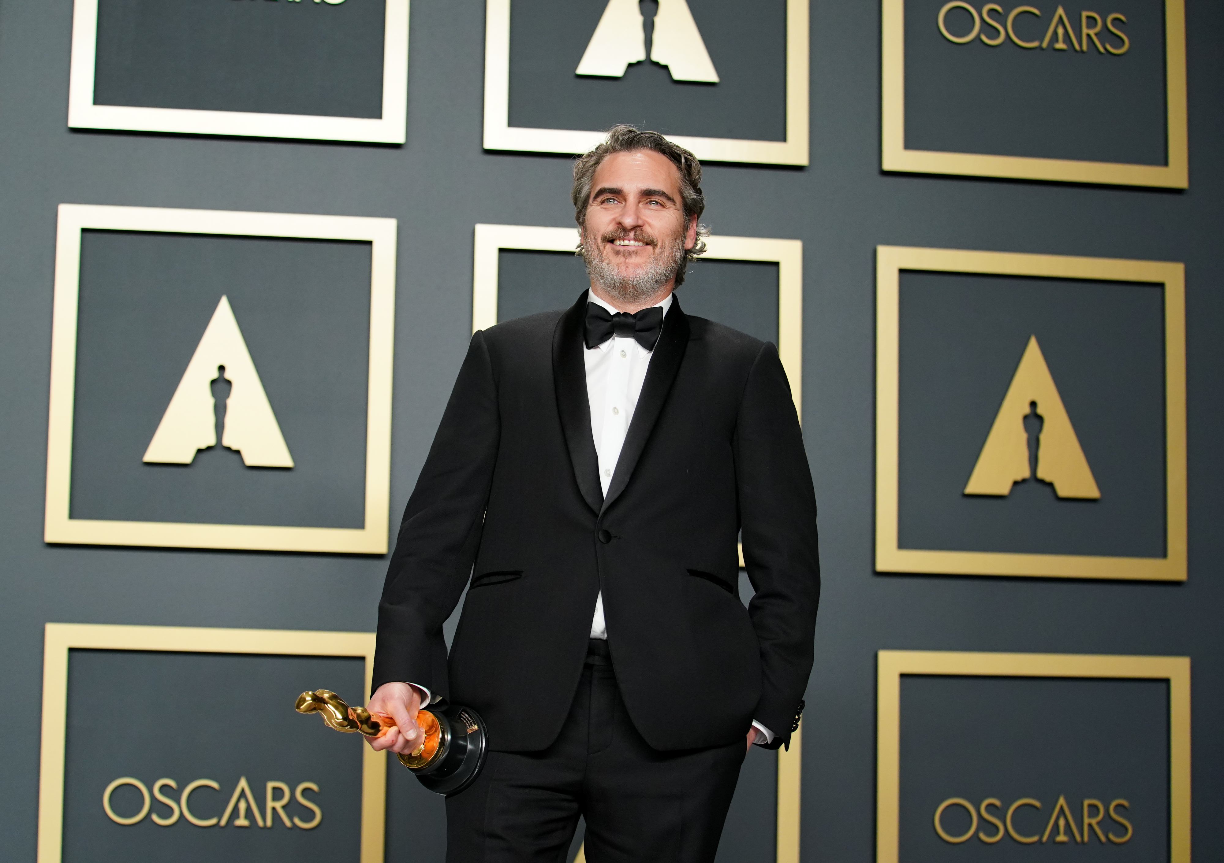 Joaquin Phoenix holds his Oscar trophy while wearing a formal black suit and bow tie at the Oscars ceremony