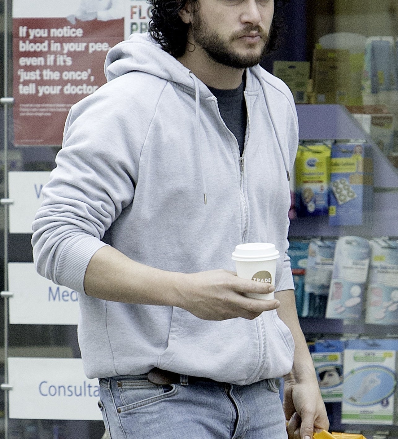 Kit Harington wearing casual clothes holds a coffee cup and Sainsbury&#x27;s shopping bag while walking outside a store