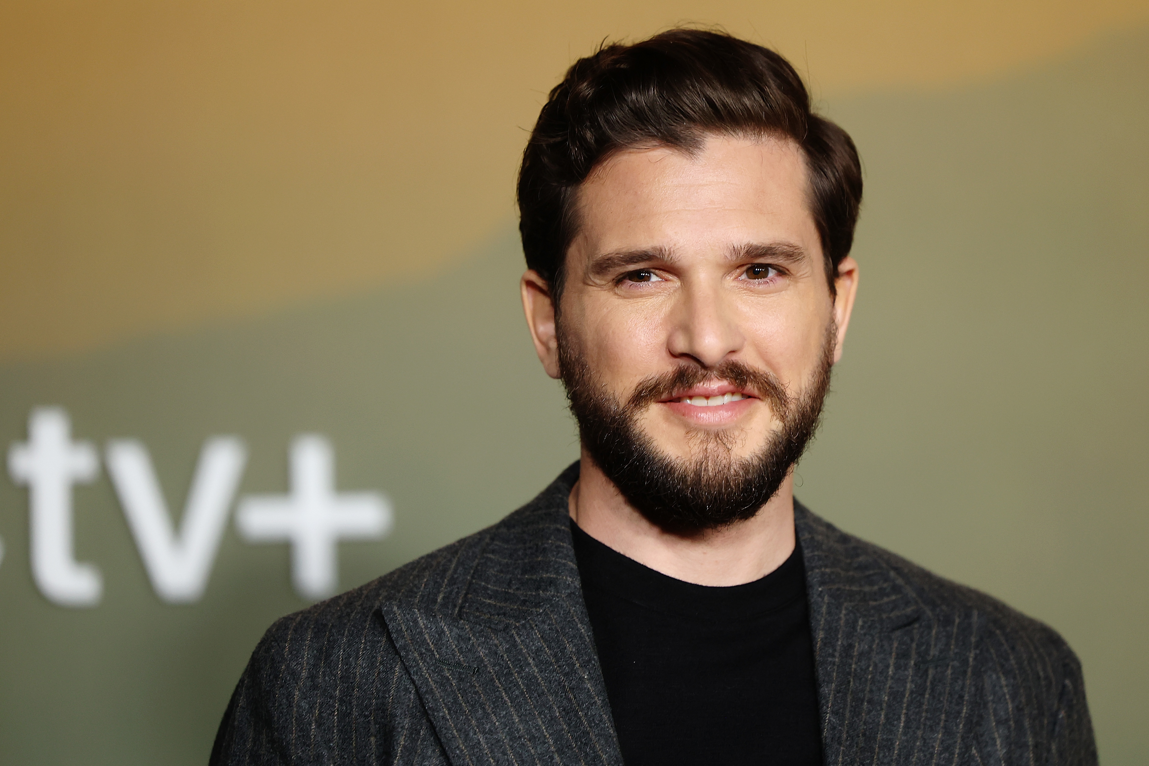 Kit Harington on the red carpet wearing a pinstripe suit with a neutral backdrop displaying an Apple TV+ logo