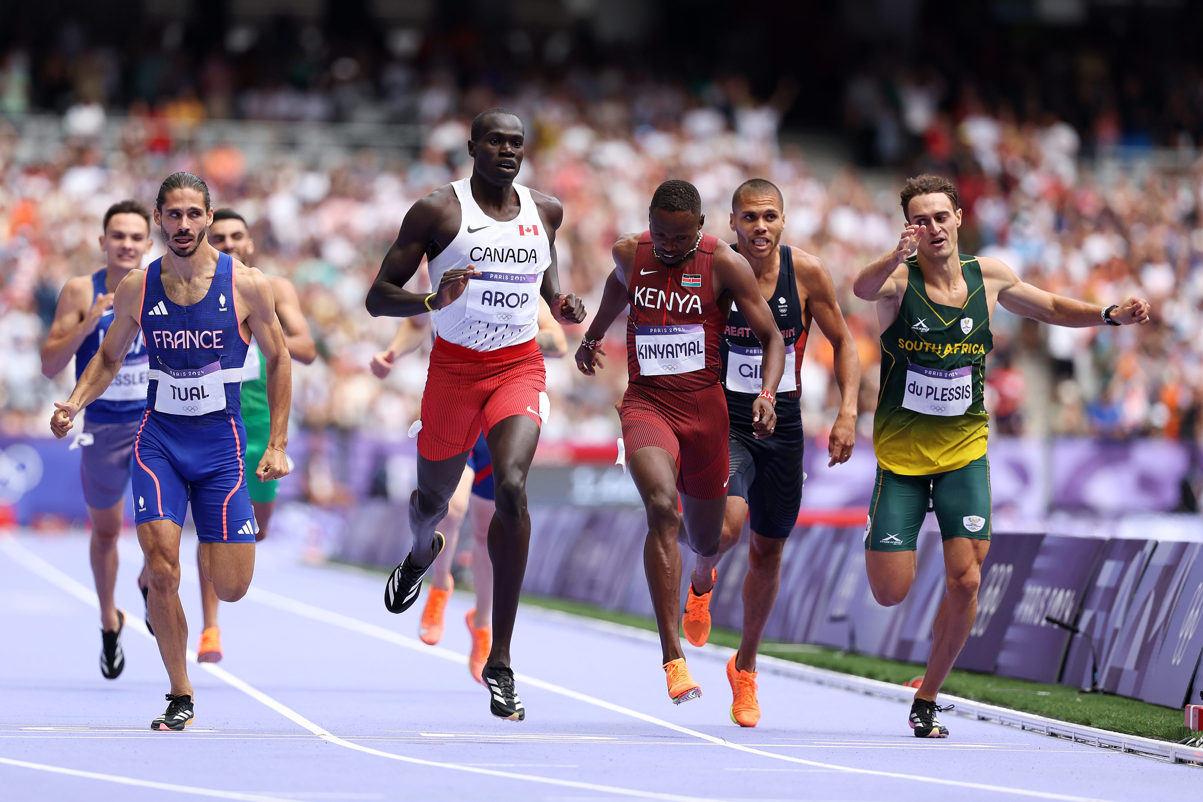 Athletes Gabriel Tual, Marco Arop, Emmanuel Korir, Adrian Ben, and others sprint near the finish line of a track race