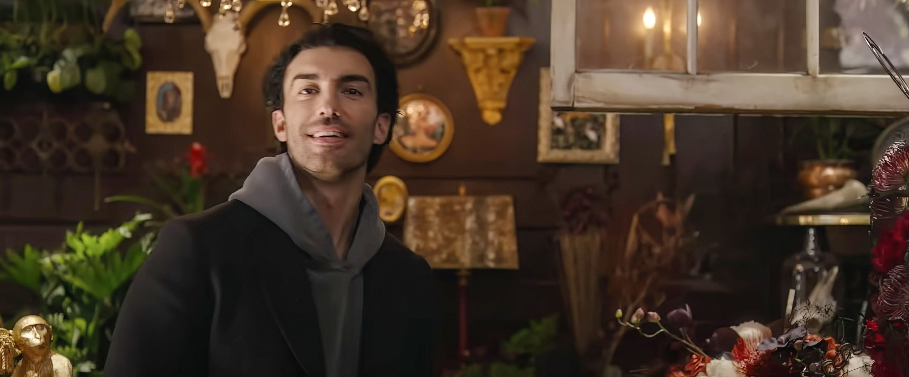 Justin Baldoni in a room with various decorations and plants, looking into the camera with a slight smile