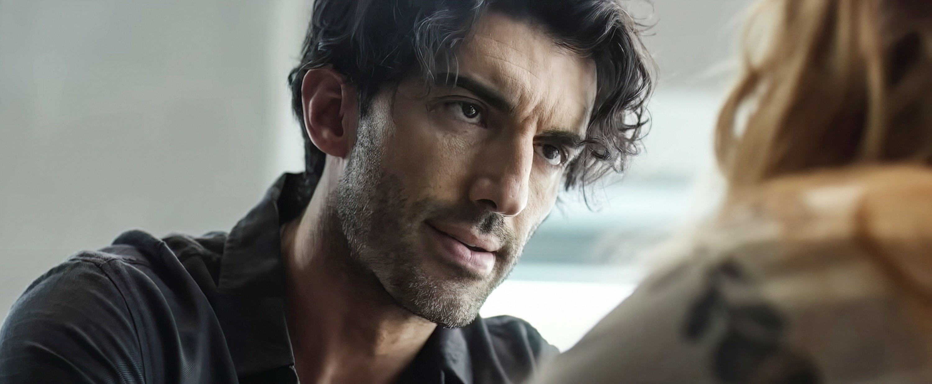 Justin Baldoni looks attentively at a blonde-haired person in a close-up scene from a movie or TV show