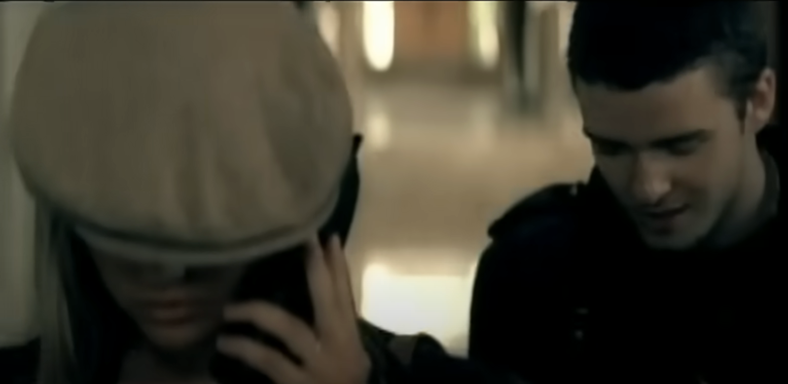 Britney Spears and Justin Timberlake walking. Britney is wearing a newsboy cap, covering her eyes slightly, and holding a phone to her ear
