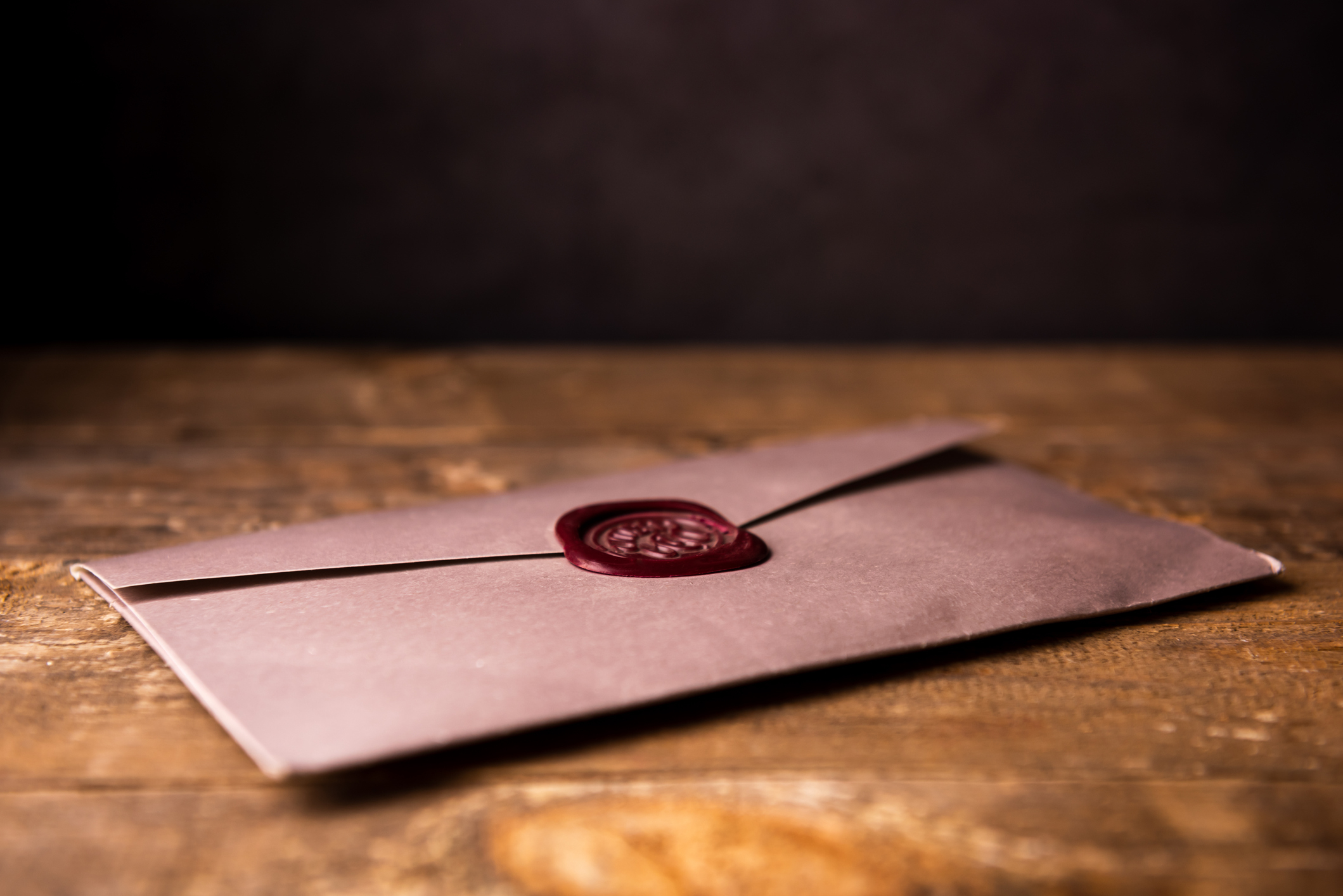 A sealed envelope with a wax seal sits on a wooden table