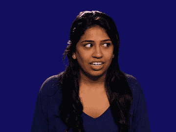 A woman with long dark hair looks to the side with an expression of surprise or confusion. She is wearing a V-neck top