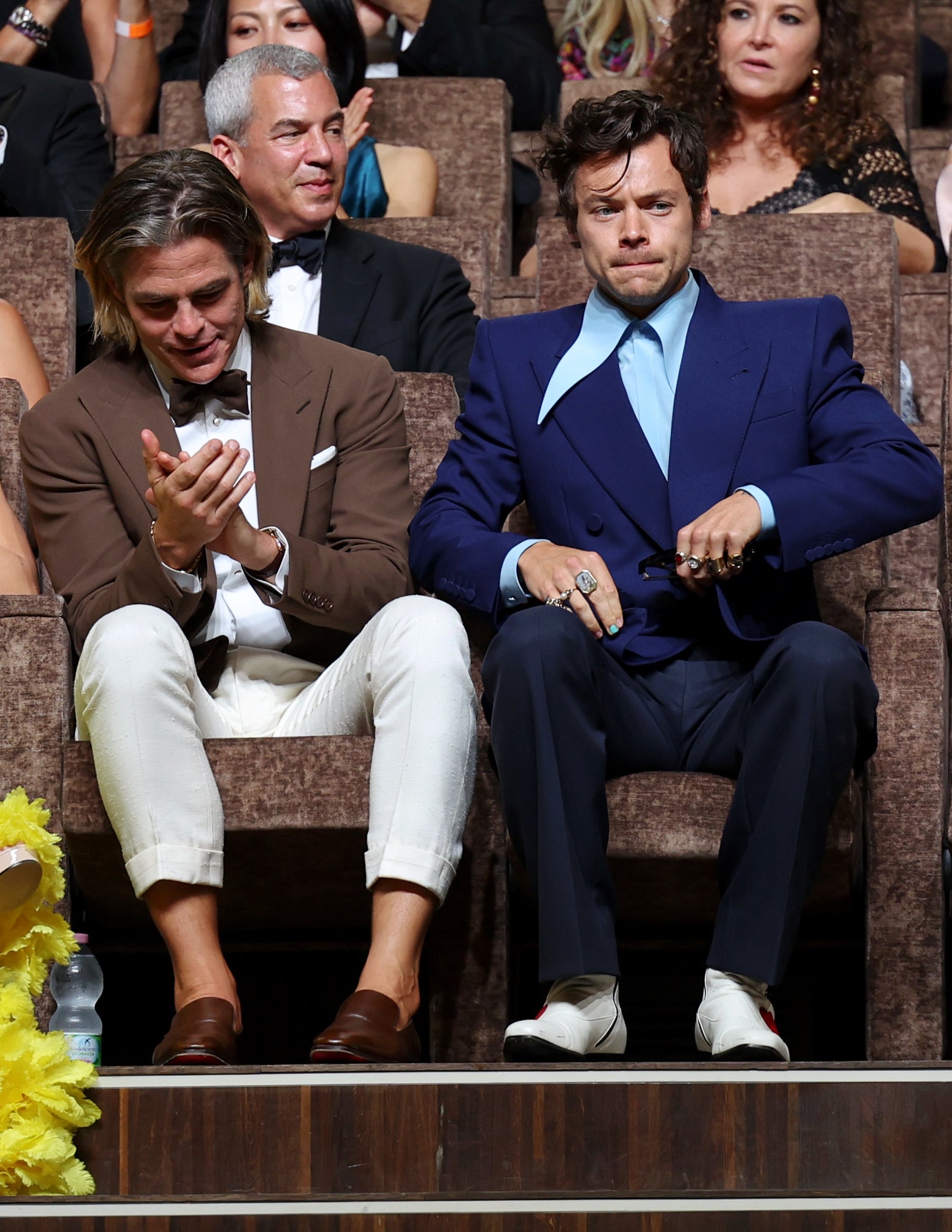 Chris Pine and Harry Styles in formal attire, seated and clapping at an event