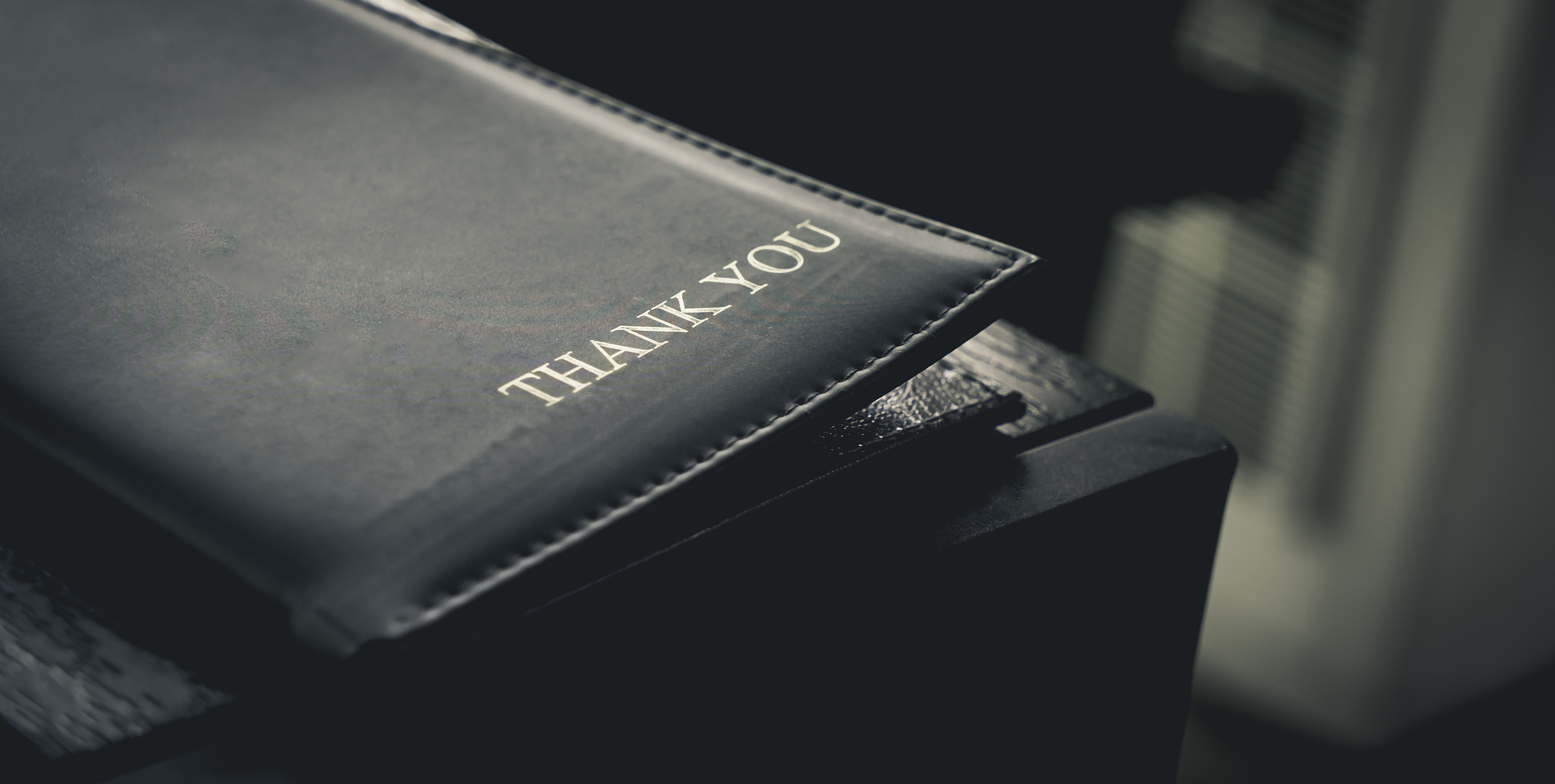 Close-up of a leather menu holder with "Thank You" written on it, placed on a dark wooden table