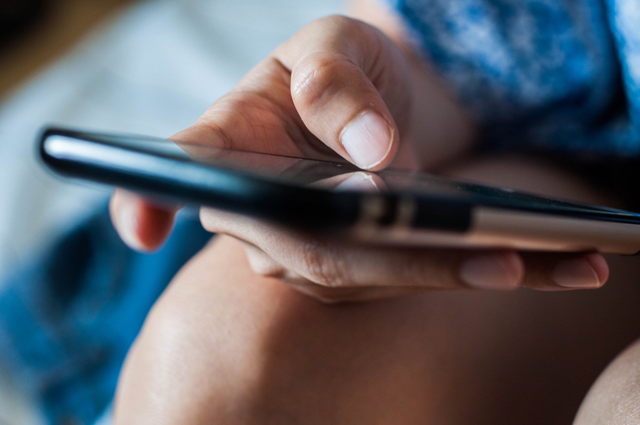 Close-up of a person's hand holding and interacting with a smartphone, focusing on their fingers touching the screen