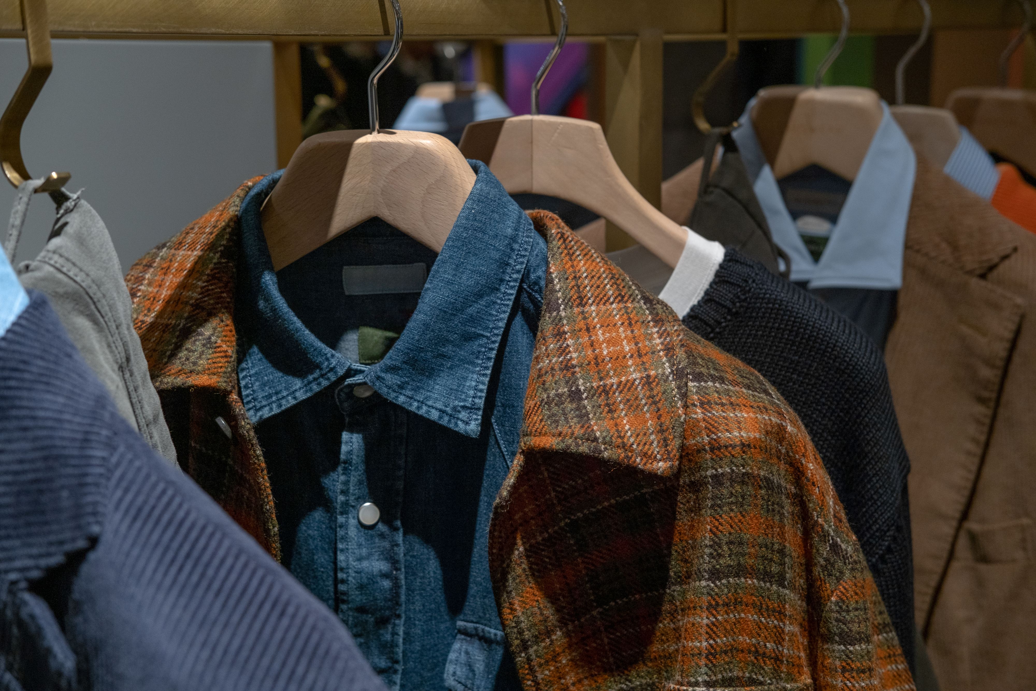 Closet with hangers holding various clothing items including a blue denim shirt, a plaid jacket, and other shirts and outerwear