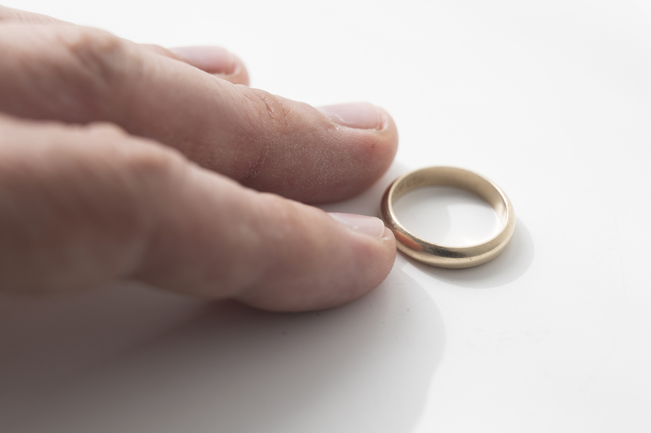 A hand with a gold wedding ring placed beside it on a light surface