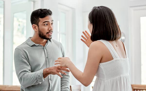 Man and woman engaged in a heated conversation in a bright indoor setting. The woman is gesturing with her hands