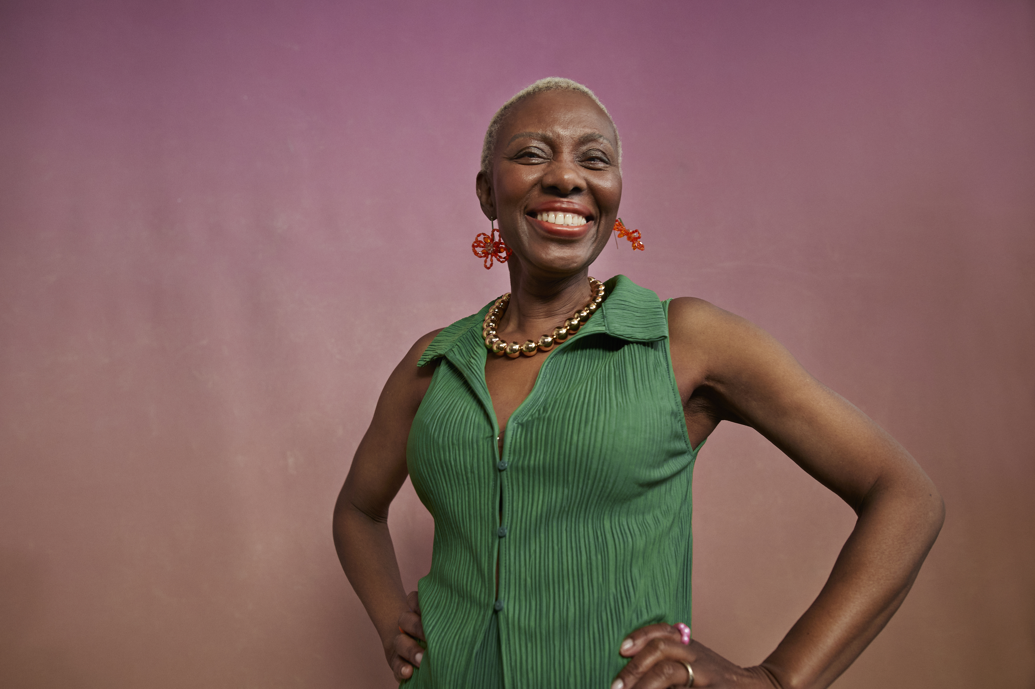 A smiling woman poses confidently against a simple background. She is wearing a sleeveless green dress and bold red earrings