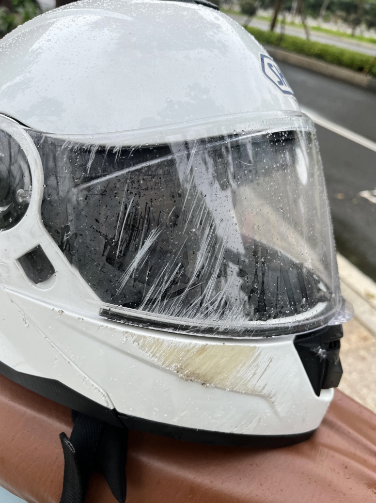 A white motorcycle helmet with a scratched visor and rain droplets sits on a surface outdoors