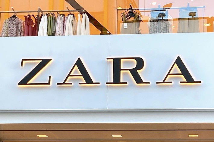 Storefront with illuminated “ZARA” sign, showcasing clothing such as shirts and jackets through large windows above