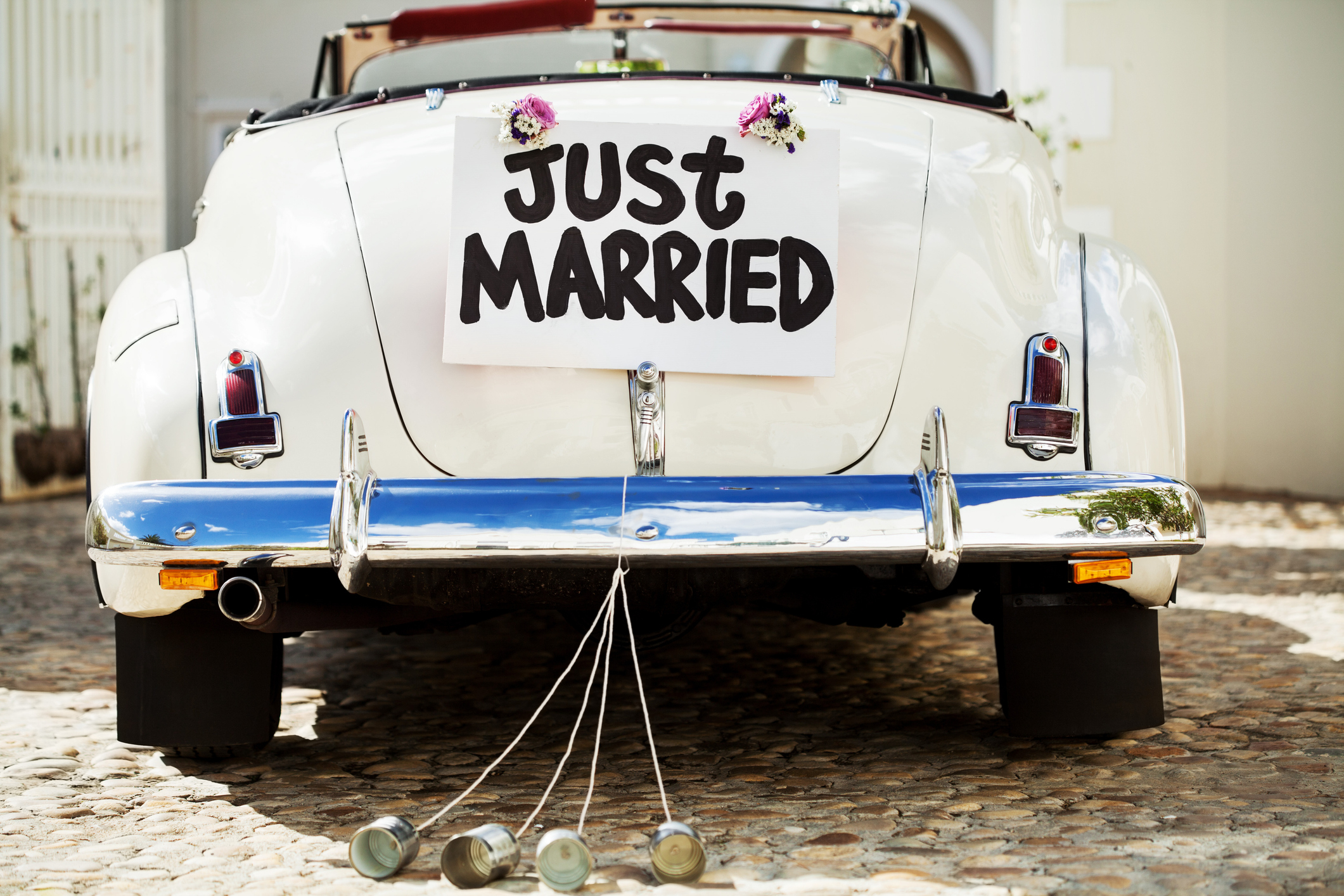 Back of a classic white car with a &quot;Just Married&quot; sign and tin cans tied to the bumper, suggesting a newlywed couple's departure