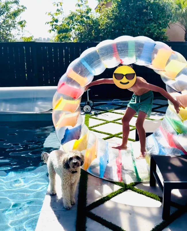 Child in swim trunks playing with a colorful inflatable in a backyard pool area