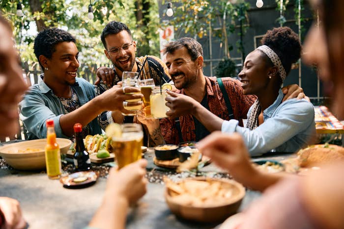 Group of friends sharing a meal outdoors, smiling and toasting with drinks