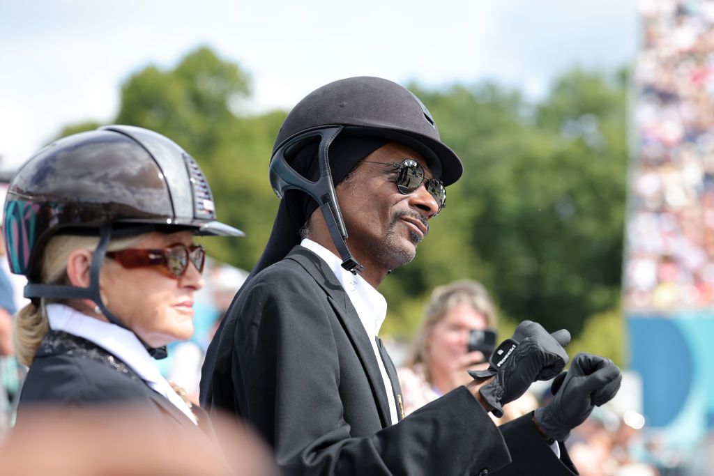 Snoop Dogg and Martha Stewart at an outdoor event, both wearing equestrian helmets and formal attire