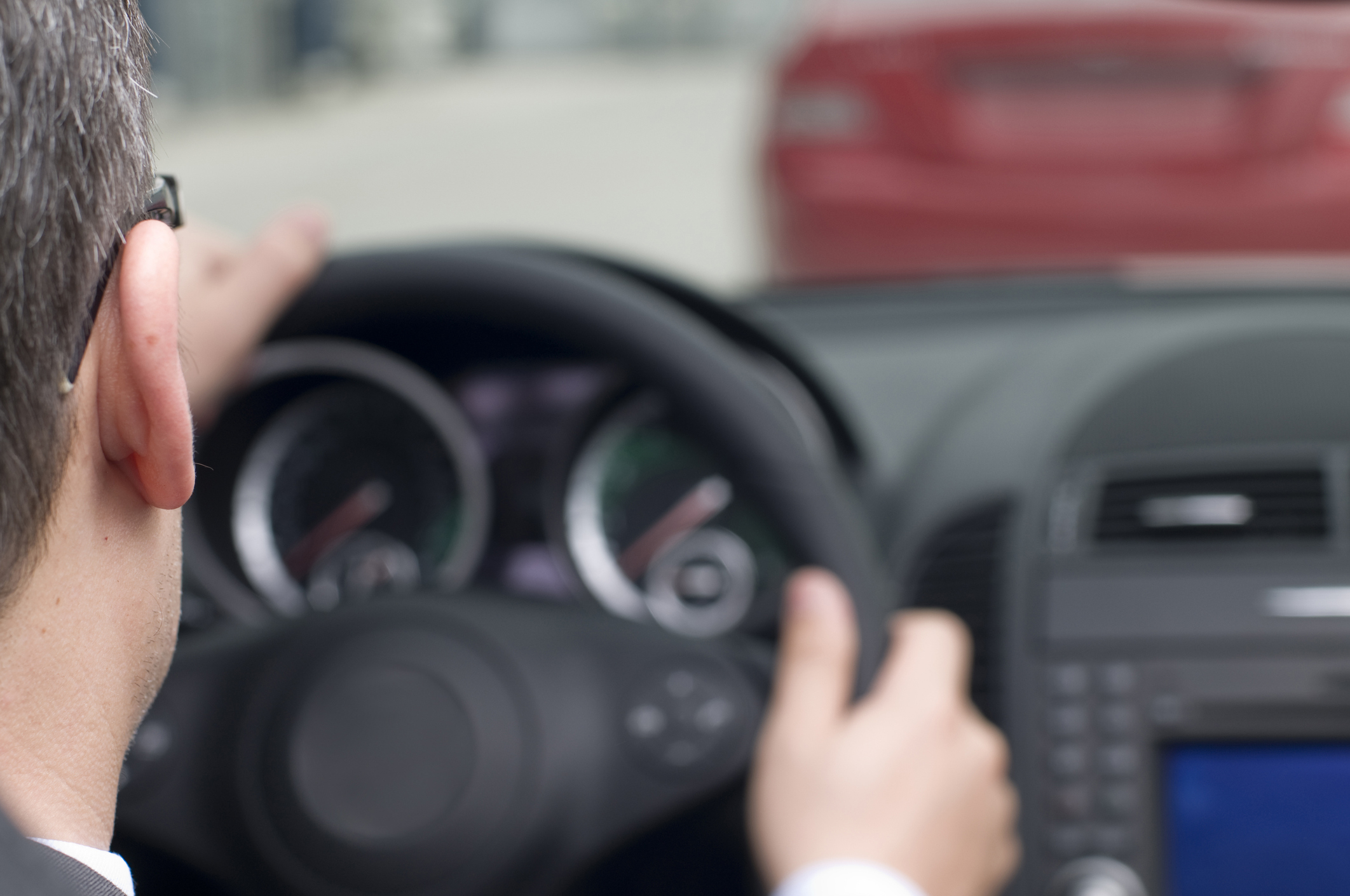 A person is seen driving a car, focusing on the road ahead with hands on the steering wheel and a dashboard in the foreground