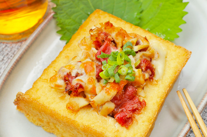 四角い揚げ豆腐の上にチーズとネギがのっている料理。旁に青じそが添えられている。