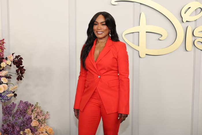 Angela Bassett in an elegant red pantsuit at a Disney event, standing in front of a floral arrangement