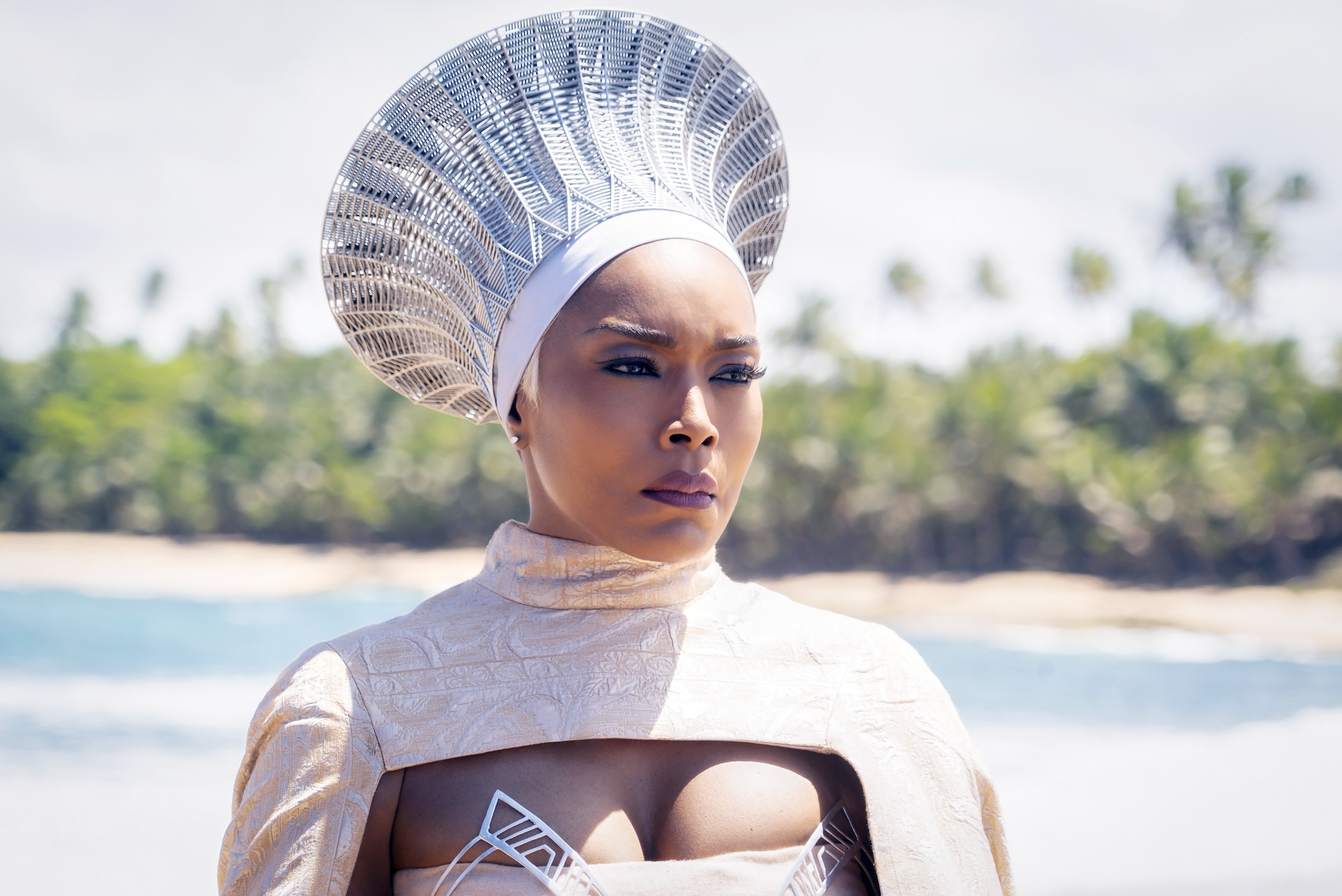 Angela Bassett in a regal, futuristic outfit with an elaborate metallic headdress, standing outdoors near a beach