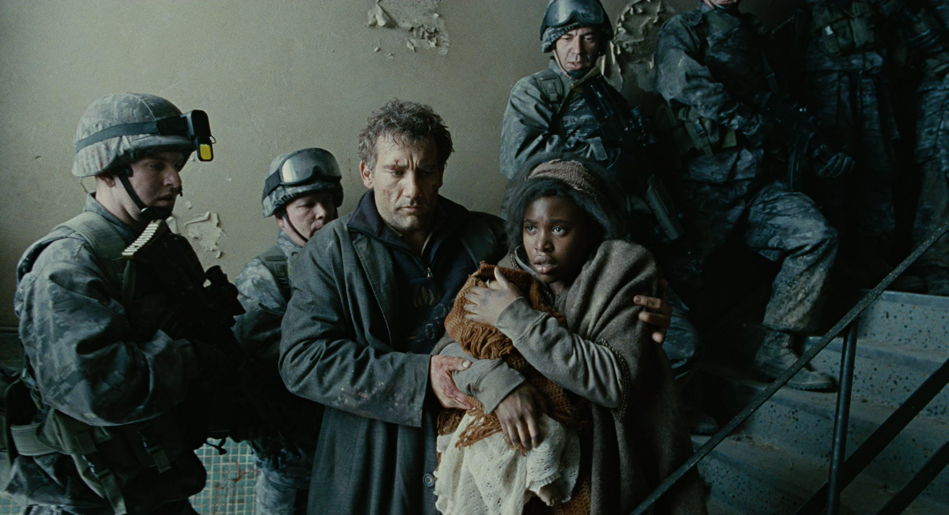 Clive Owen and Clare-Hope Ashitey stand on a stairway, surrounded by soldiers in tactical gear, as Clive supports Clare-Hope, who cradles a baby