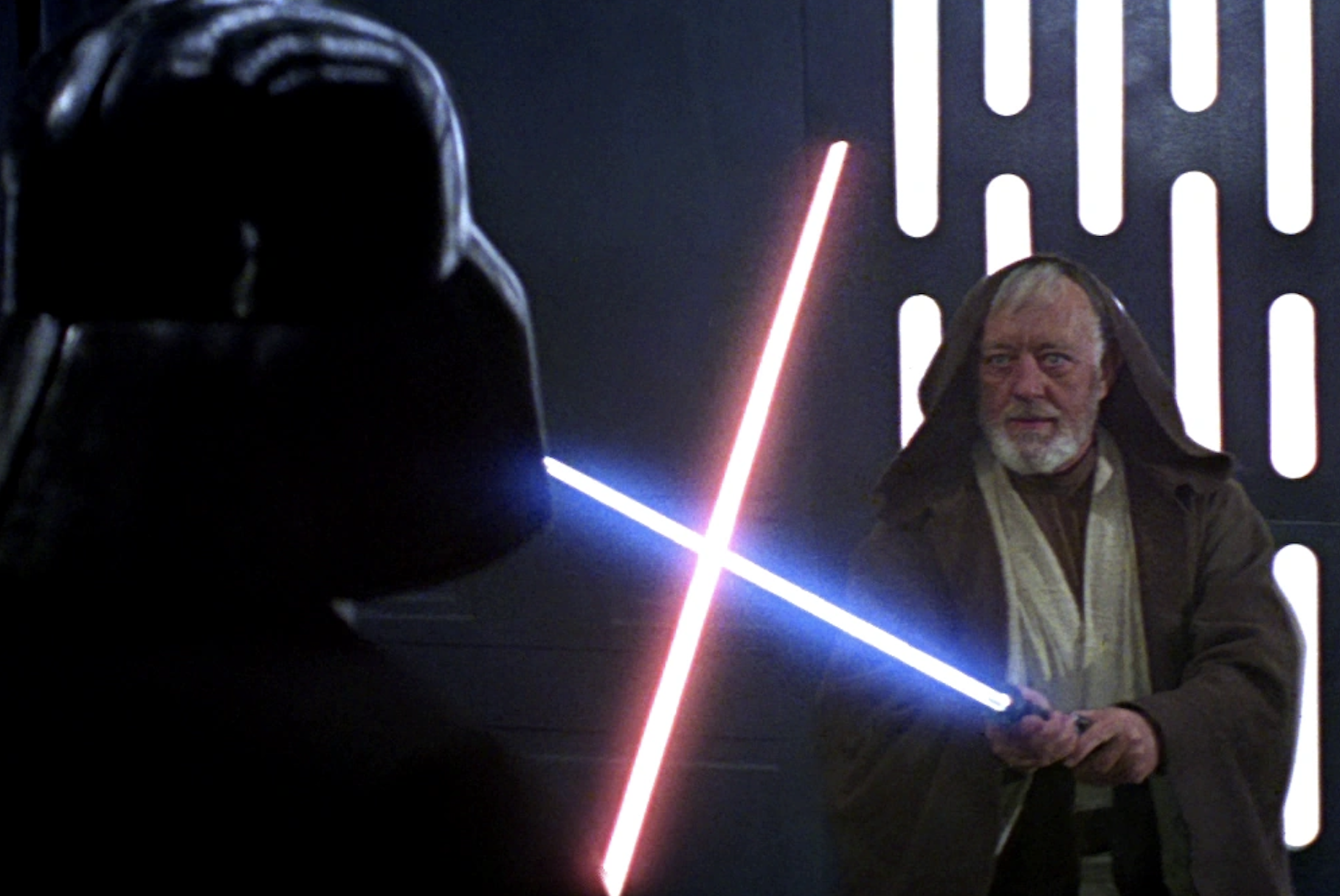 Darth Vader and Obi-Wan Kenobi face off with lightsabers in a scene from "Star Wars: A New Hope". Vader's saber is red, and Obi-Wan's is blue