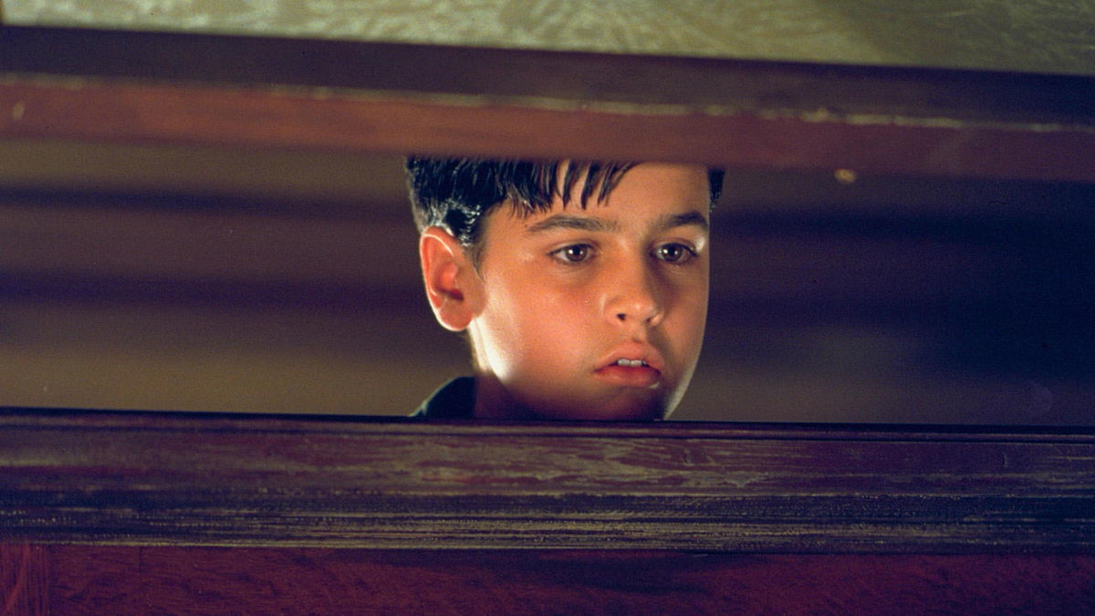 A young boy peers through a slightly opened door with a curious expression