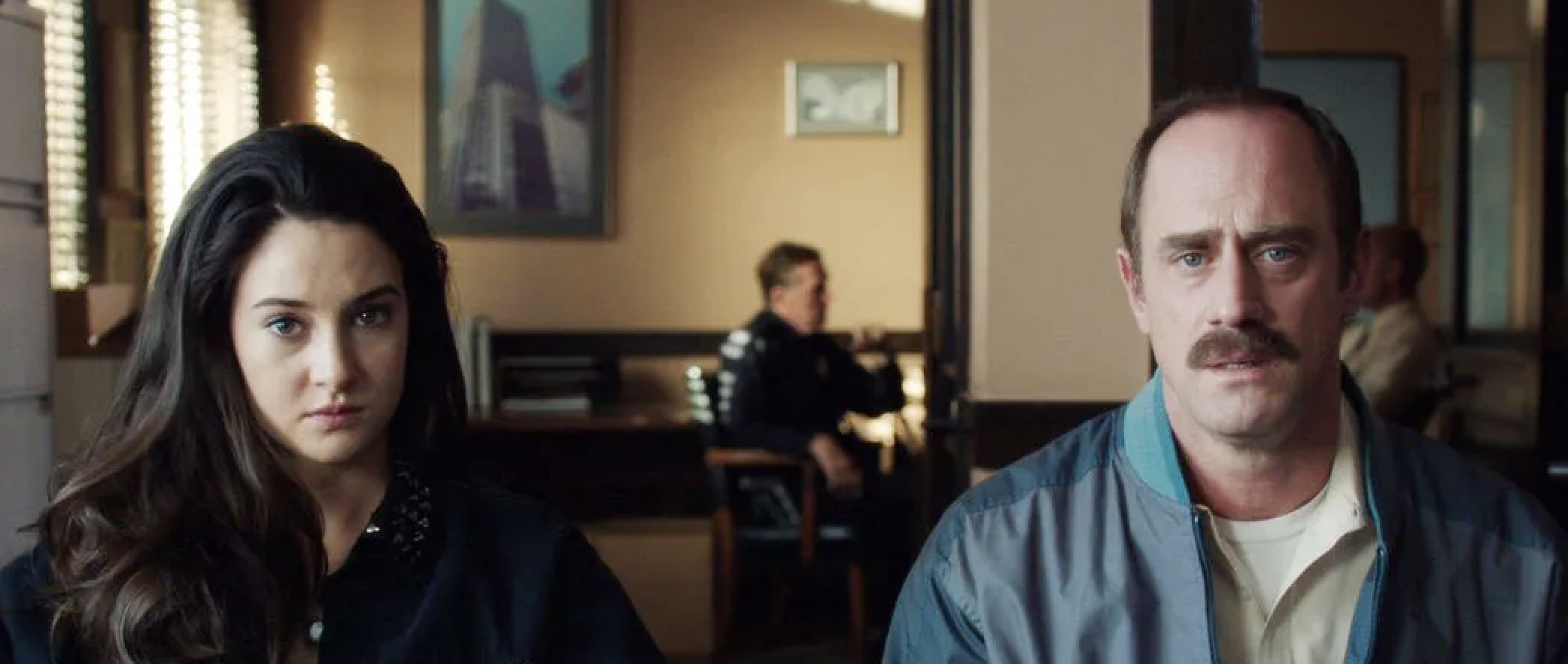 Shailene Woodley and Christopher Meloni sit looking serious in an office setting with a police officer in the background