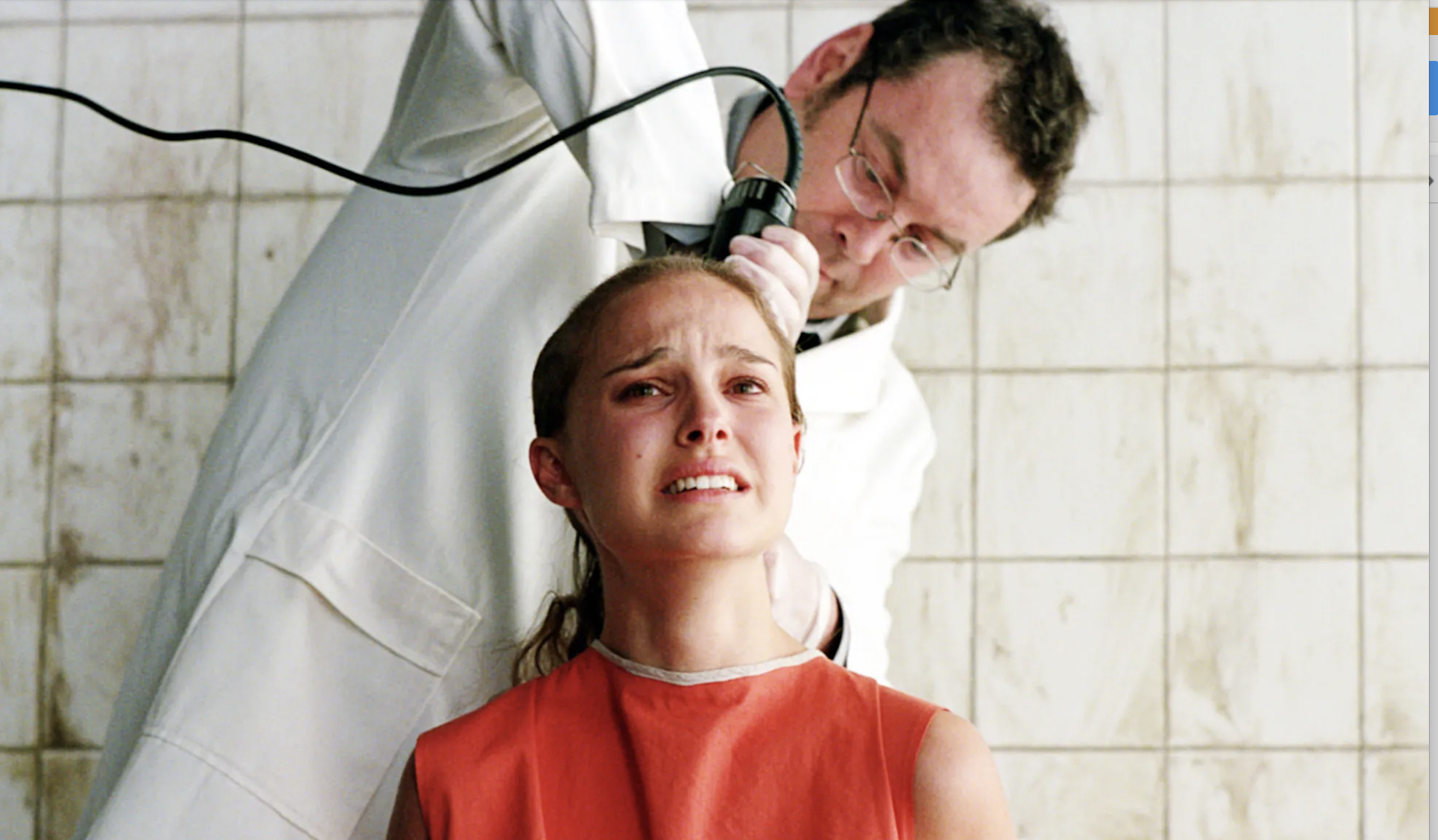Natalie Portman is seen with a distressed expression as a person in white cuts her hair in a tiled room