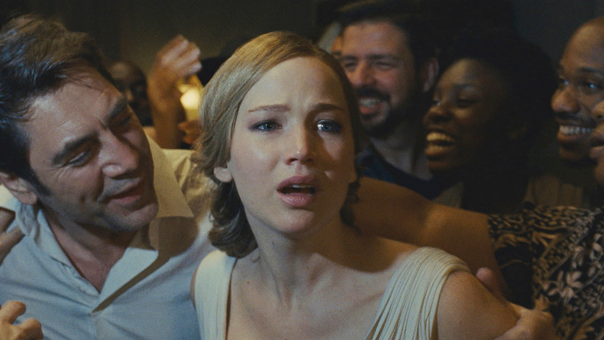 Jennifer Lawrence, surrounded by people, appears distressed while Javier Bardem and others crowd around her, reaching out with friendly gestures