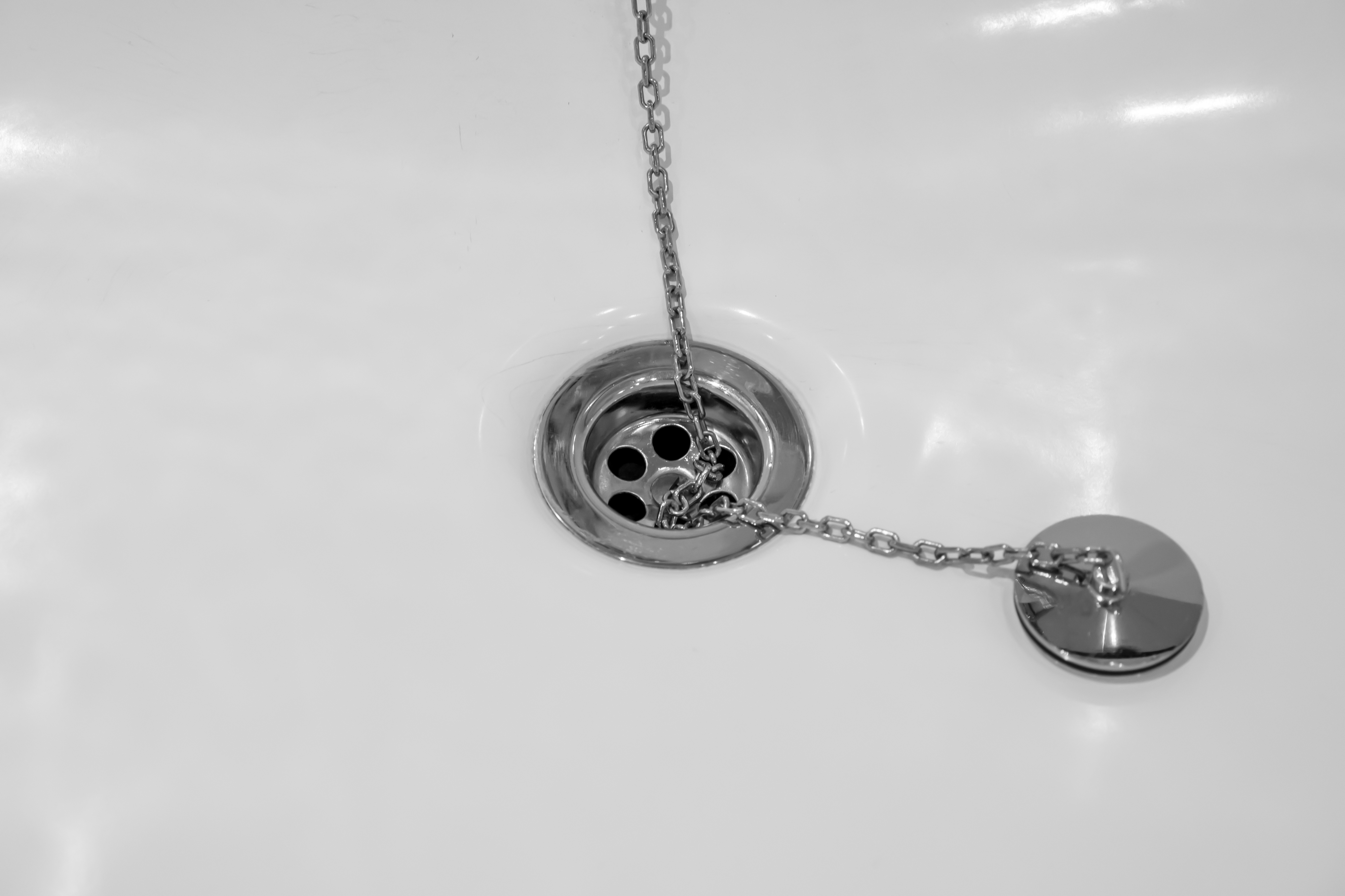 Close-up of a bathtub drain with a chain attached to the plug resting nearby