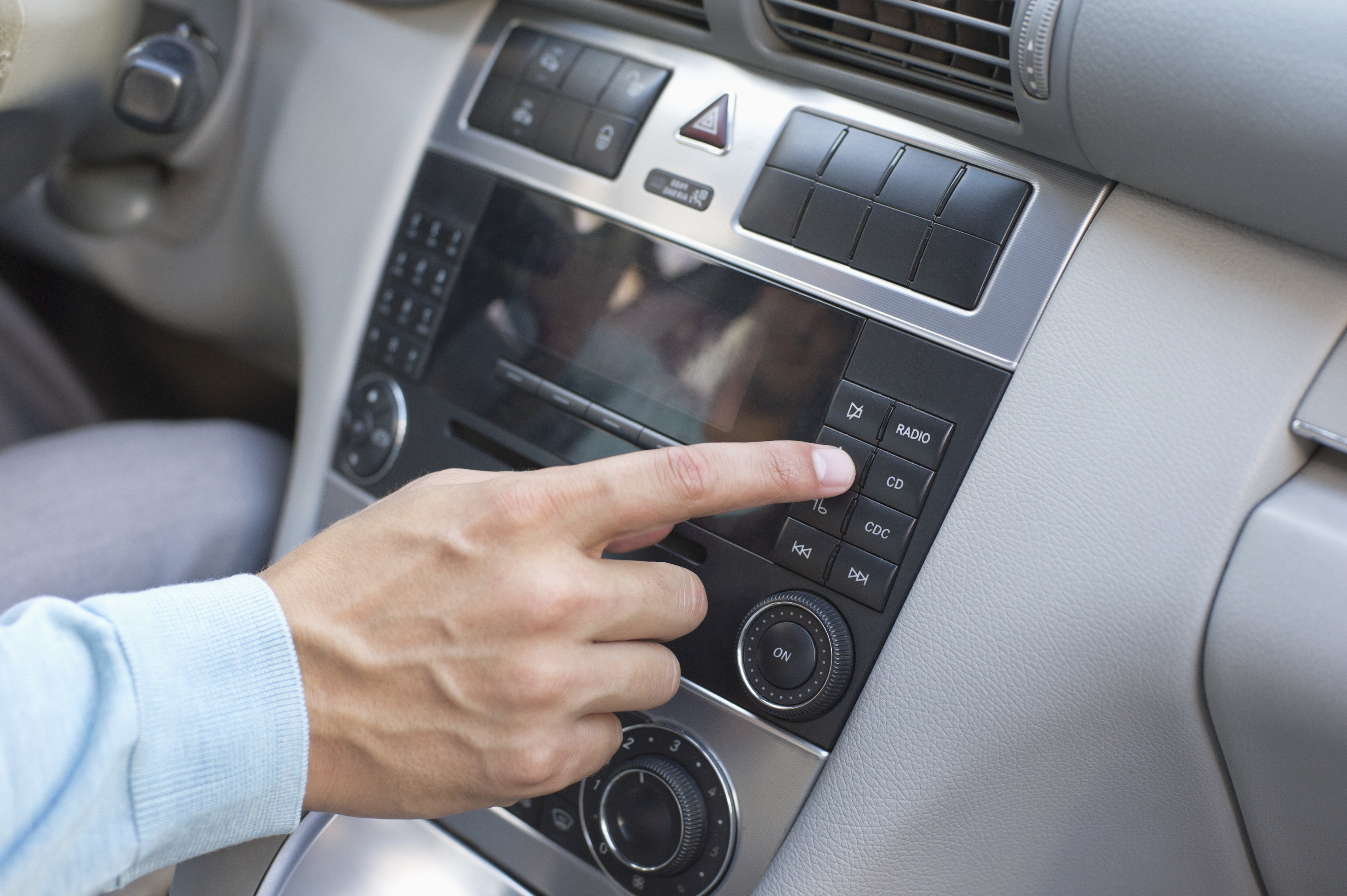 A person’s hand selects a button on a car's audio system dashboard, highlighting features like radio, CD, and AUX