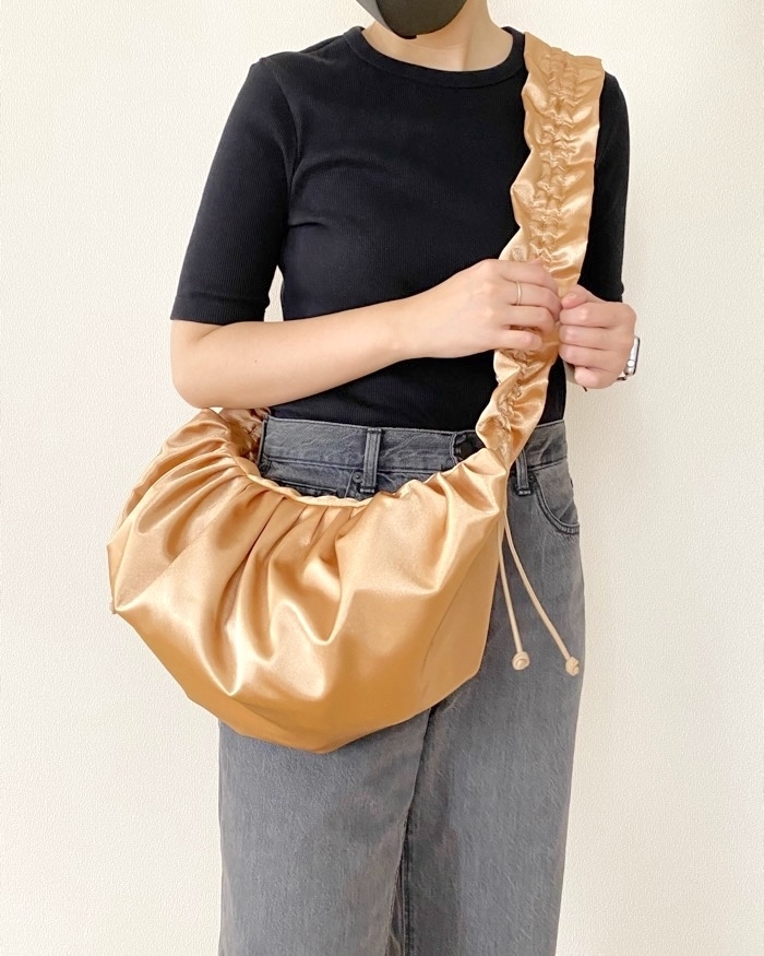 Person in dark top and jeans holds a shiny, ruched shoulder bag with one hand on the strap and one on the bag