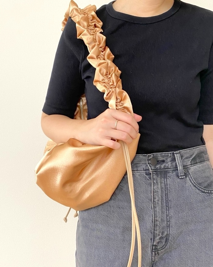Person wearing a black top, high-waisted jeans, and holding a gold, ruffled shoulder bag. Face not visible