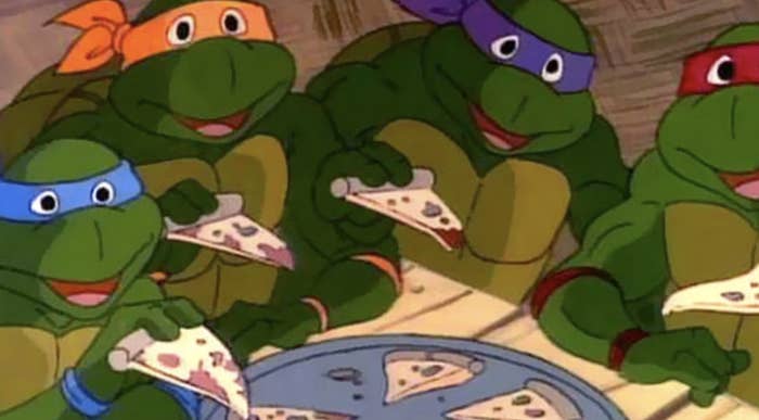 Leonardo, Michelangelo, Donatello, and Raphael from Teenage Mutant Ninja Turtles enjoy slices of pizza around a table