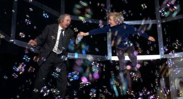 Gene Wilder in a suit holds Peter Ostrum's hand as they float surrounded by bubbles in a scene from "Willy Wonka & the Chocolate Factory."