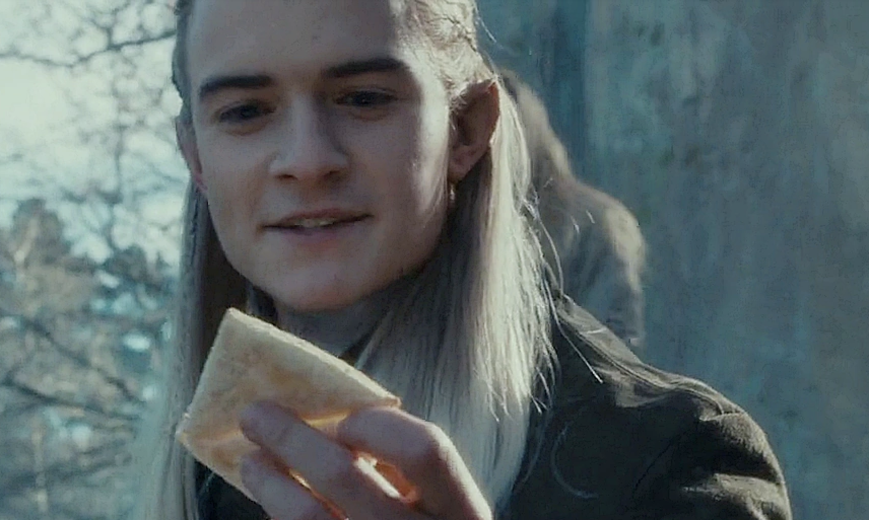 Orlando Bloom as Legolas in "The Lord of the Rings" smiling and holding a piece of lembas bread outdoors