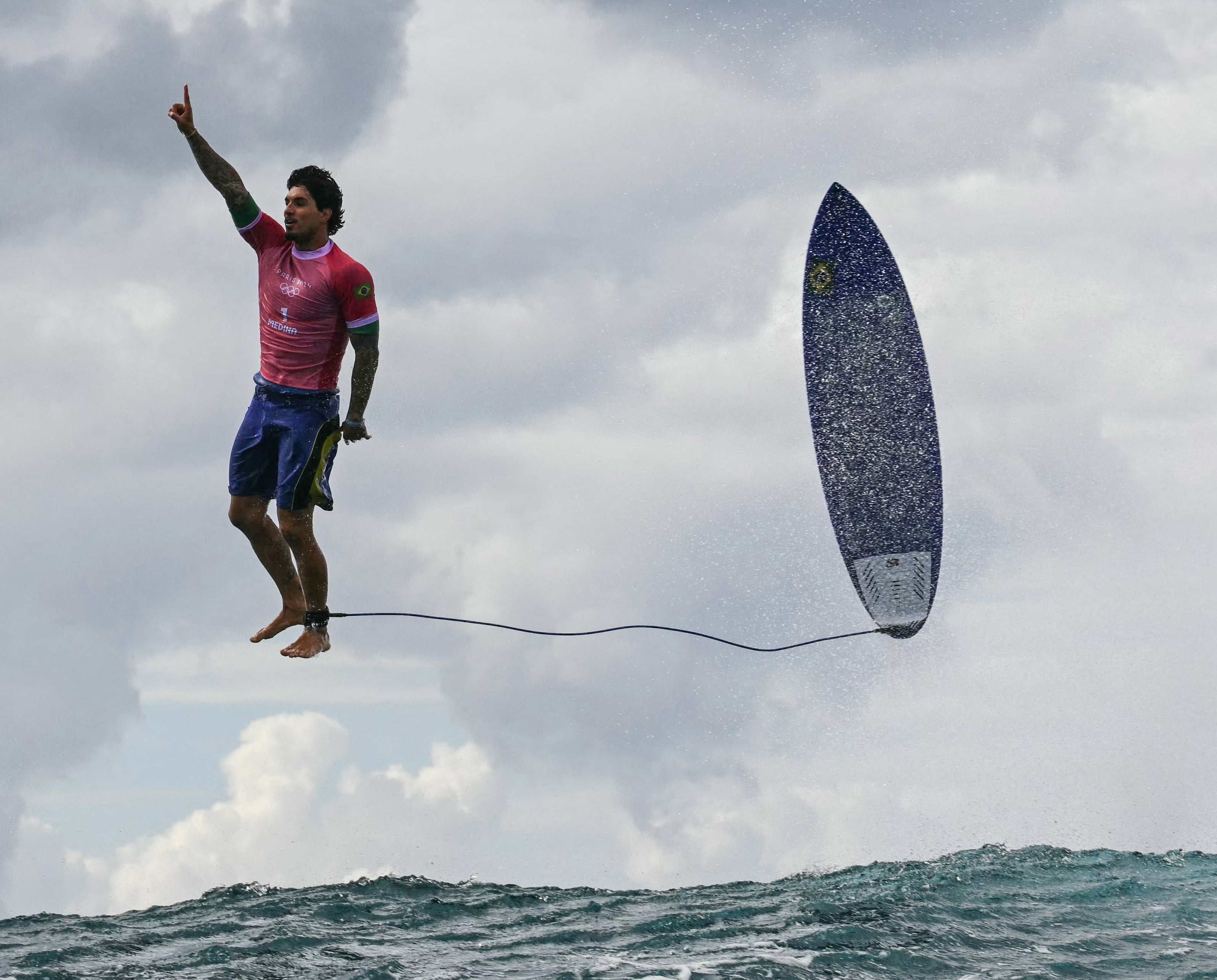 A surfer performs an impressive maneuver above the wave, with the surfboard mid-air next to him