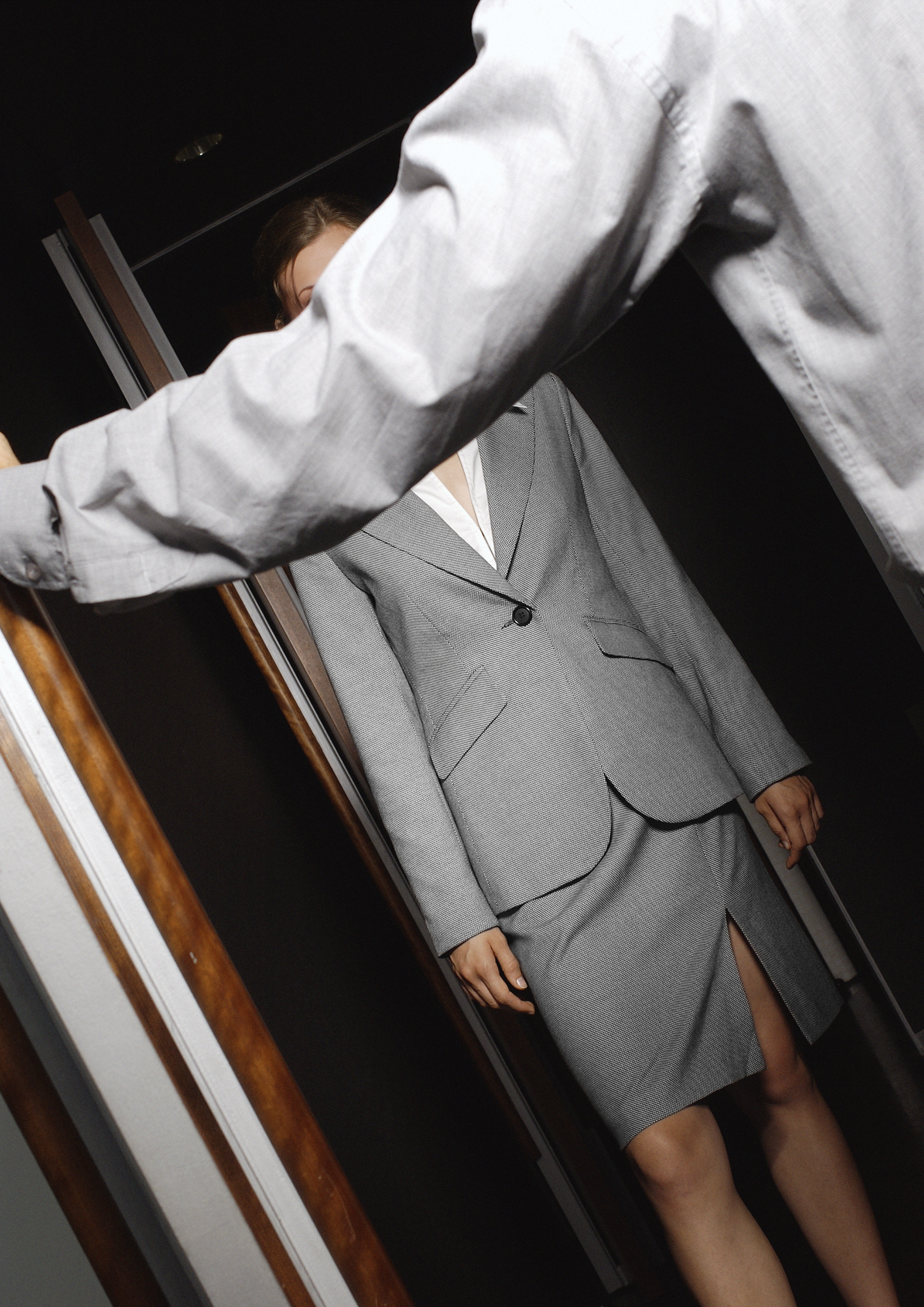 A person is holding a door open for a woman wearing a gray business suit and skirt