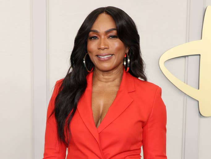 Angela Bassett in a stylish, fitted suit, poses for a photo on the red carpet. She accessorizes her look with hoop earrings and wears her hair down