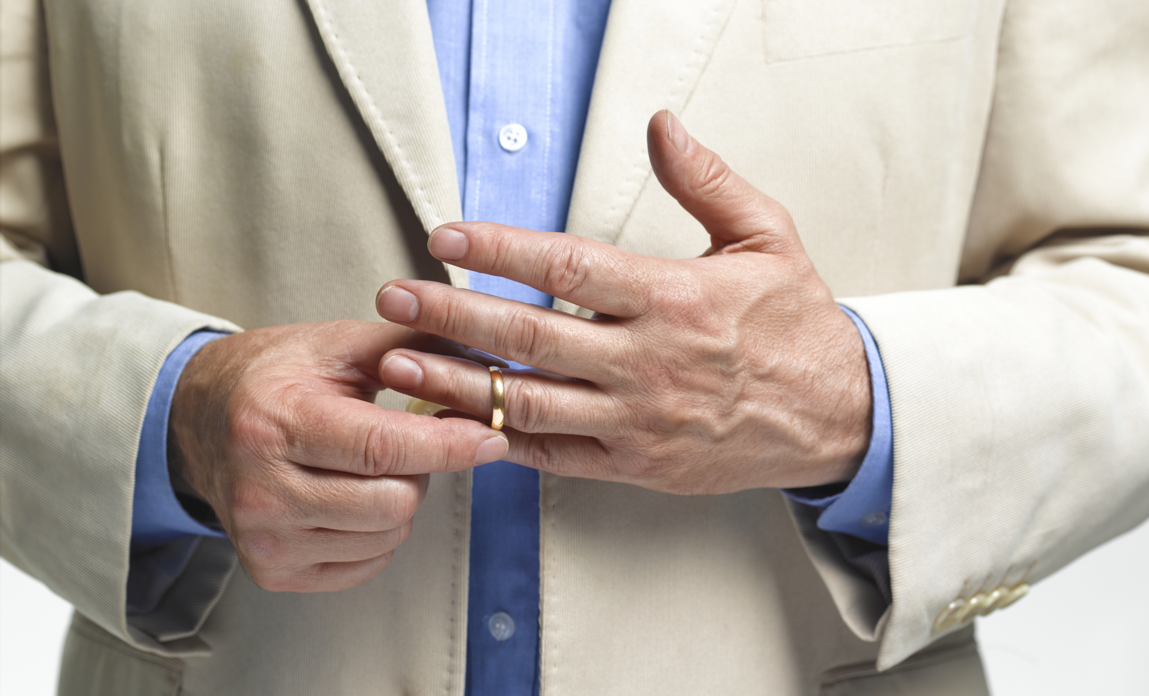A person wearing a light blazer and blue shirt is in the process of removing a gold ring from their left hand