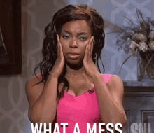 A woman in a pink dress from SNL holds her head with both hands, expressing distress. The text on the image reads, &quot;WHAT A MESS.&quot;